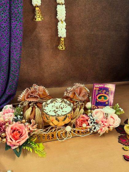 A simple yet elegant Diwali hamper on a golden tray. It features a bowl of sweets and two potlis, all brought together with a beautiful floral arrangement.