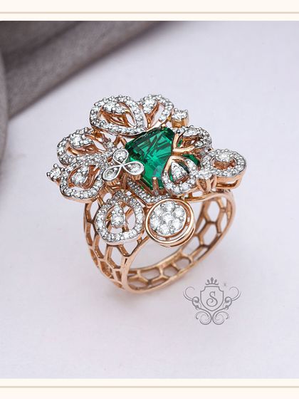A true work of art, this statement ring features a large, square-cut green gemstone surrounded by an elaborate floral design of diamonds and rose gold. The honeycomb pattern on the band adds a modern, structural element.