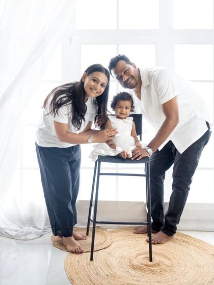 A fun and interactive family pose, with the parents leaning in towards their daughter who is seated on a stool.