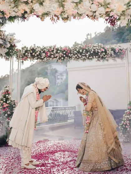 A moment of mutual respect and tradition at a scenic mountain wedding. The couple greets each other under a beautiful floral arch, with the vast hills providing a serene backdrop for their ceremony.