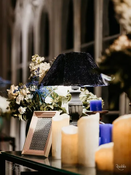 A close-up of a table lamp with a crushed velvet shade, surrounded by candles and flowers. This detail from the 'Gothic Palace Ball' Sangeet contributed to the moody and luxurious atmosphere.
