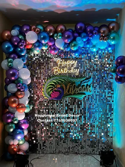 I can create themed backdrops based on your ideas. This birthday setup features a silver sequin wall with a custom peacock feather nameplate and a garland of chrome balloons in multiple colors.