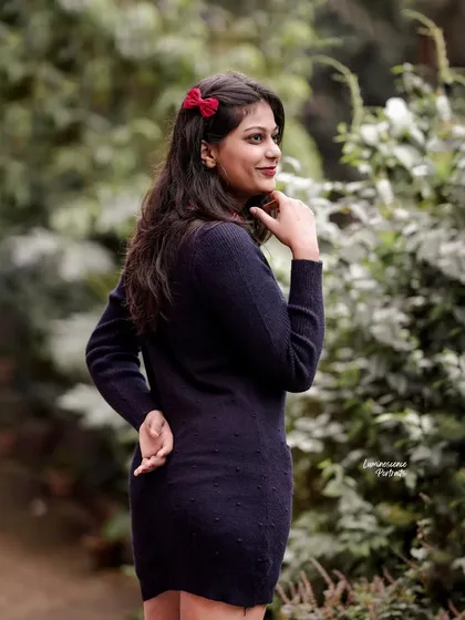 A three-quarter portrait in a garden setting, the red bow in the model's hair adds a pop of color to her classic black dress.