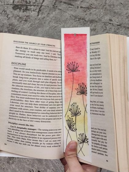 For those who love nature, I paint bookmarks with delicate floral illustrations. This design features minimalist dandelion-like flowers against a warm pink and yellow watercolour wash, bringing a soft, gentle touch to your book.