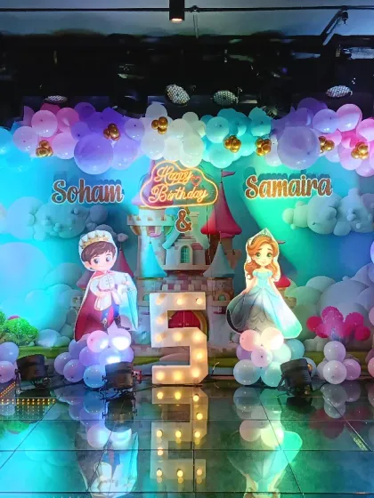 The main stage for a grand princess and prince themed birthday. The setup includes a large balloon backdrop, character cutouts, and a giant light-up number "5" on a reflective floor.
