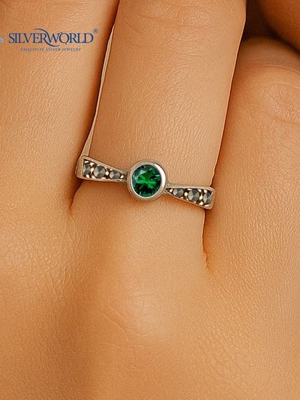 This elegant ring features a central green emerald, flanked by dark marcasite stones on a twisted silver band. It's a delicate yet colorful statement.