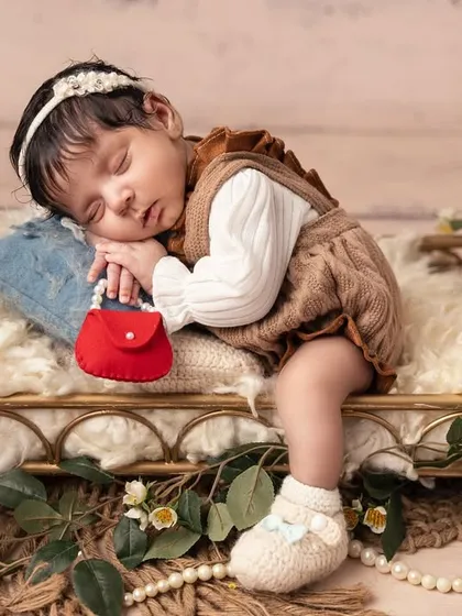 A little princess sleeping on a miniature golden bed, surrounded by delicate greenery. The tiny red purse adds a pop of color to this enchanting, fairy-tale scene.