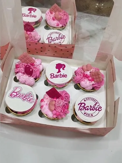 A box of custom Barbie-themed cupcakes, perfect for a birthday girl. Each cupcake is 100% eggless, with some featuring detailed edible prints and others topped with pink frosting, sprinkles, and chocolate pieces for a truly magical look.