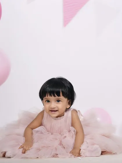 All smiles during this first birthday studio session. The simple setup with pink balloons and a festive banner keeps the focus on the baby's joyful personality.
