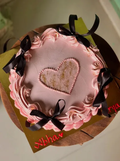 A pretty pink cake with a shimmering gold heart center, framed with piped swirls and black ribbon bows.