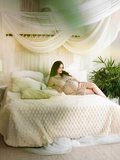 A dreamy and serene lifestyle shot. The mom-to-be relaxes on our beautifully styled studio bed, creating a peaceful and intimate portrait.
