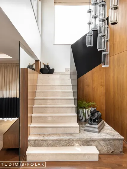The same staircase, showing its elegant proportions and the beautiful contrast between the light marble, dark railing, and warm wood wall. It's a perfect example of a transitional space designed with intention.