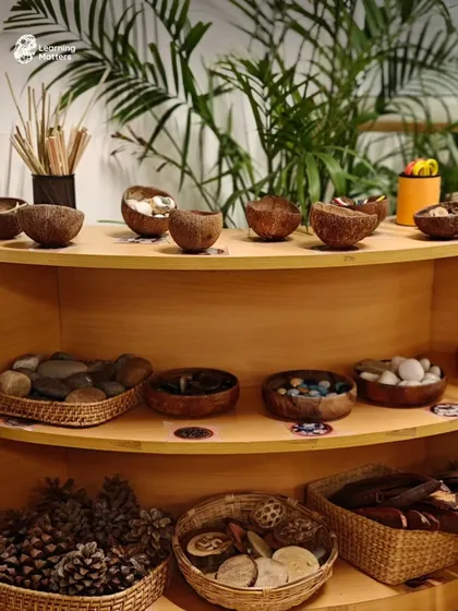 Our environment is the third teacher. We intentionally curate shelves with natural, open-ended materials like stones, pinecones, and seed pods. These "loose parts" invite children to imagine, create, and construct their own stories, transforming simple objects into anything their minds can conceive.