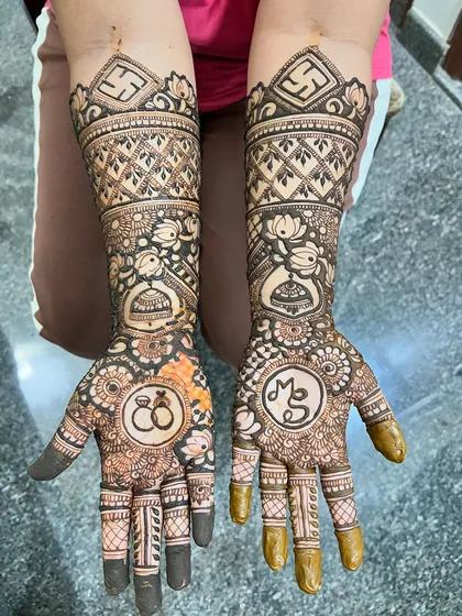 This engagement mehendi for Madhushree features her initials 'MS' and a drawing of her engagement rings, surrounded by jhumkas and auspicious swastika symbols.