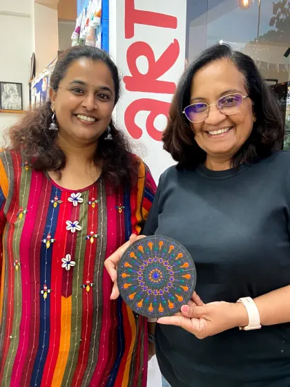 Two friends with their finished dot mandala art. The process of creating these intricate patterns is both relaxing and rewarding.