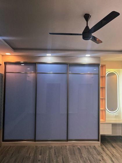 Floor-to-ceiling wardrobes help maximize storage and make a room look larger. This design features back-painted glass sliding shutters and an integrated dresser with a backlit mirror.