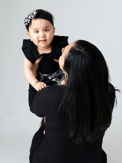 A mother lifts her baby girl high in the air against a clean, grey studio backdrop. This simple setting is perfect for capturing playful, interactive moments.