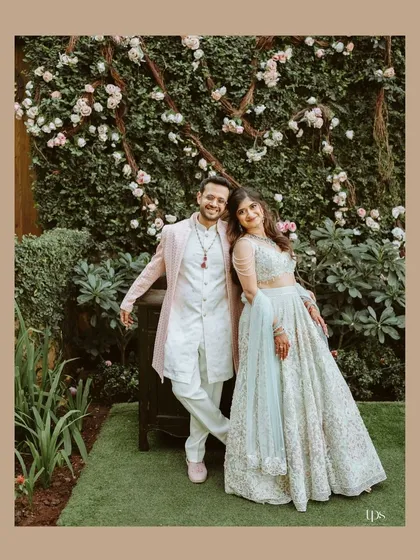 A relaxed portrait of Avi and Devika against a wall of flowers. Their casual poses and happy expressions create a warm and inviting image.