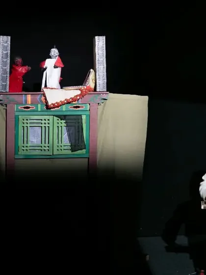 A performer plays a traditional Korean instrument alongside a puppet show in 'Hong Dongji & Isimi'. The live music is integral to this slapstick performance.