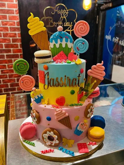 A vibrant two-tier candyland cake that's a feast for the eyes. It's decorated with edible ice cream cones, lollipops, macarons, and donuts, making it the ultimate sweet dream for a colorful birthday party.