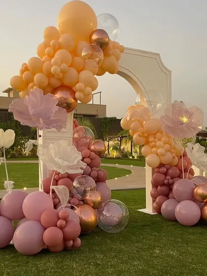 A stunning balloon arch in shades of peach, pink, and rose gold, accented with large, ethereal paper flowers, creating a perfect photo backdrop for a bridal shower.
