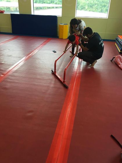 A father and coach work together to help a child practice on a mini bar, showing how we partner with parents to support their child's journey.