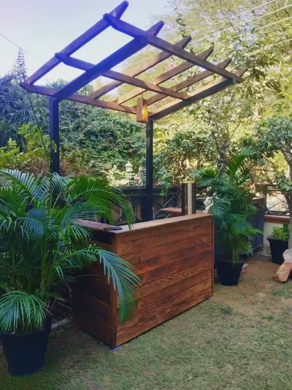 A simple yet elegant wooden bar counter with a small pergola, perfect for a garden or backyard setting.