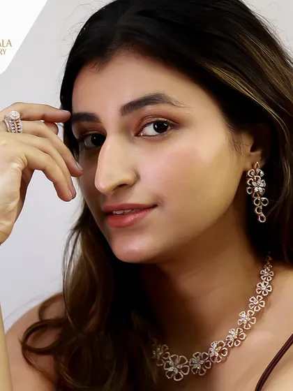 A model wears a complete floral-themed diamond set in rose gold, including a necklace, earrings, and ring.
