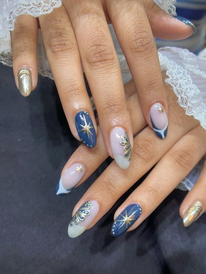 This elegant design features hand-painted gold stars and intricate fan-like patterns over a deep blue and sheer base. It's a sophisticated take on celestial nail art.