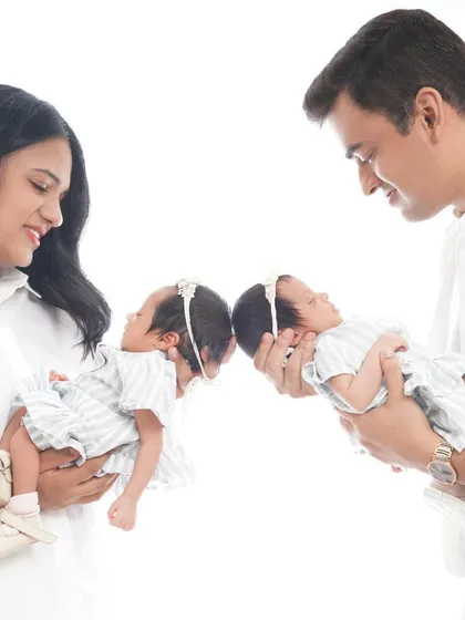 A creative portrait of parents holding their twin newborn daughters, bringing their heads together to show their special connection.