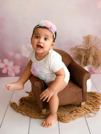 A baby girl kicks her leg up with a happy expression during her sitter session.