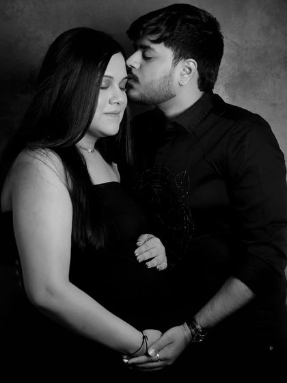 A romantic black and white portrait. The husband's gentle kiss on his wife's forehead and their shared embrace make for a deeply emotional and classic maternity photograph.