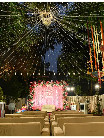 A wide view of an outdoor evening event, with a canopy of fairy lights creating a starry sky. The setup is ready for an evening of performances and celebration under the lights.