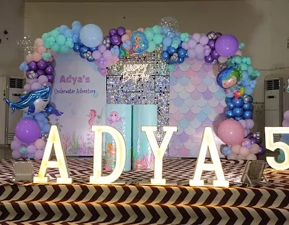 We dove deep to create Adya's underwater adventure for her fifth birthday. This setup features a mermaid-scale sequin backdrop, balloon arrangements in ocean hues of aqua and purple, and character cutouts to bring her under-the-sea dream to life.