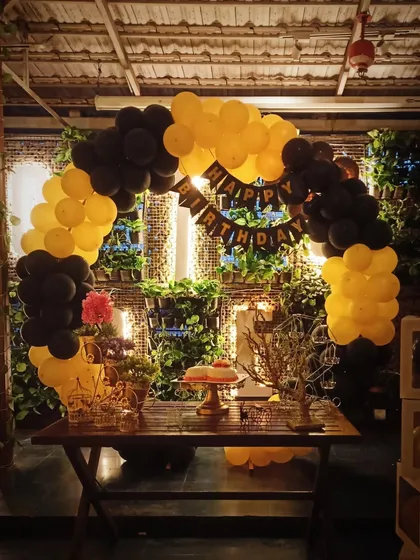 A modern and stylish balloon arch in a striking yellow and black color scheme. Set against a natural green wall, this setup includes a 'Happy Birthday' banner and transparent 'BABY' blocks for a chic, contemporary feel.