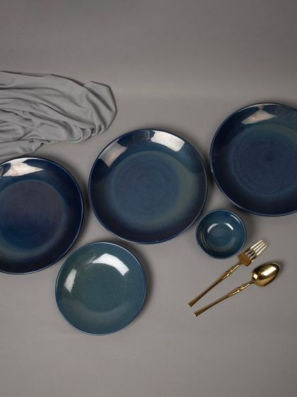 A flat-lay of a blue ceramic dinnerware set, showing various plate and bowl sizes.