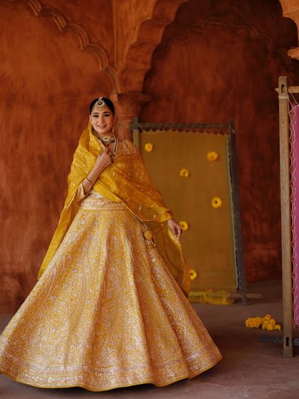 Golden hour goodness. This full-length shot shows off a magnificent yellow lehenga, perfect for a Haldi or Mehendi, with makeup that glows in the warm light.