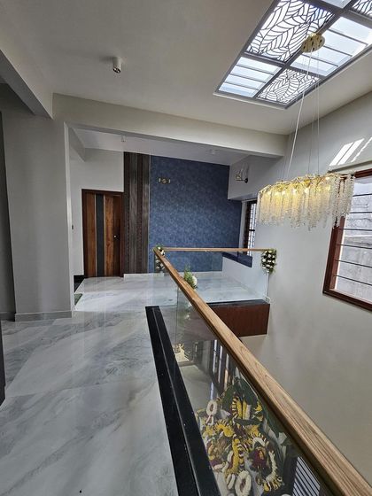 A view of the upper floor in a newly constructed villa, showcasing the glass and wood railing, marble flooring, and a stunning chandelier. The design focuses on creating a sense of height and luxury.