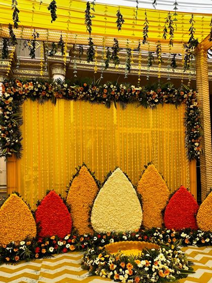 This traditional Haldi backdrop features a vibrant yellow curtain and teardrop-shaped panels made entirely of fresh marigold and tuberose flowers, set against a cheerful yellow and white chevron floor.
