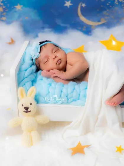 A peaceful newborn dreams amongst the stars and clouds in this creative celestial-themed setup, complete with a tiny bed and a knitted bunny friend.