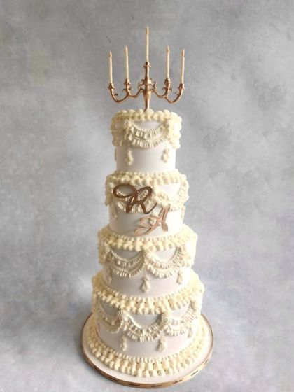 For this beautiful wedding, we created a four-tier cake with traditional Lambeth piping. The topper was a custom-made candle stand, inspired by the chandelier at the venue, to make it truly personal for the couple.