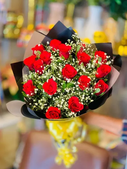 A lush bouquet of classic red roses and baby's breath. The contrast of the deep red petals against the tiny white flowers is timeless, and the black wrapping adds a touch of modern elegance.