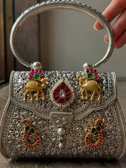 An example of my detailed craftsmanship on a pure silver clutch. This piece features intricate filigree work and is adorned with custom motifs, including gold-plated camels and colourful Kundan work, making it a true statement accessory.