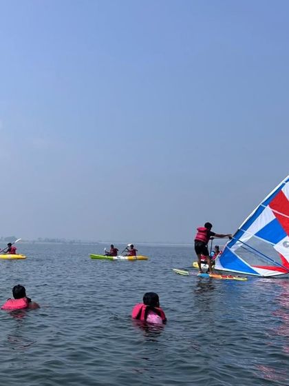 A windsurfer glides past a group of swimmers, showcasing one of the many activities in our basic aqua sports course.