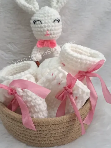 A beautiful baby gift hamper with a bunny rattle and booties, all tied with delicate pink ribbons and arranged in a woven basket.