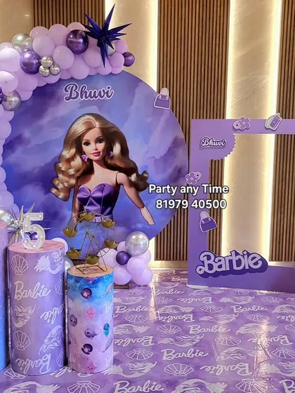 A Barbie theme party in purple. This setup includes a large character backdrop, a balloon arch, themed pedestals, and a fun photo frame prop.