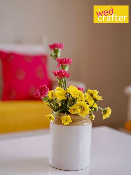 A simple, elegant detail from the Haldi event, with a traditional pickle jar used as a vase for bright yellow and pink flowers.
