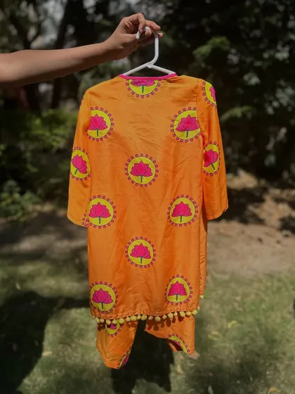 A close-up of the orange lotus-print kurta. You can see the soft fabric and the playful pom-pom details along the hem.