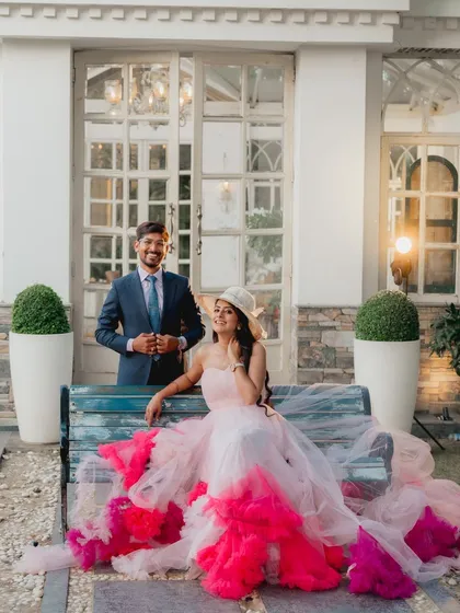 The couple poses on a bench, with the bride's vibrant, trailing gown creating a stunning visual. This shot is full of color, style, and personality.