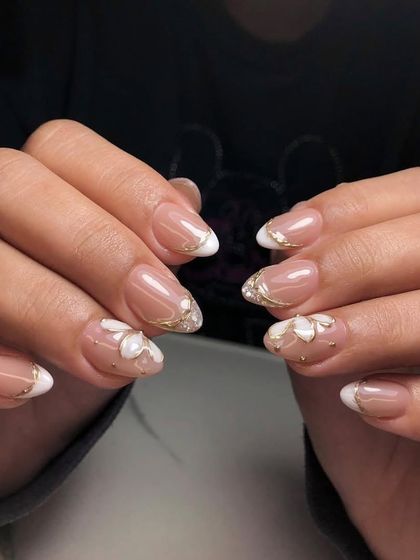 A delicate and elegant design. These almond nails have a nude base with white French tips, accented with 3D flowers and fine gold line art.
